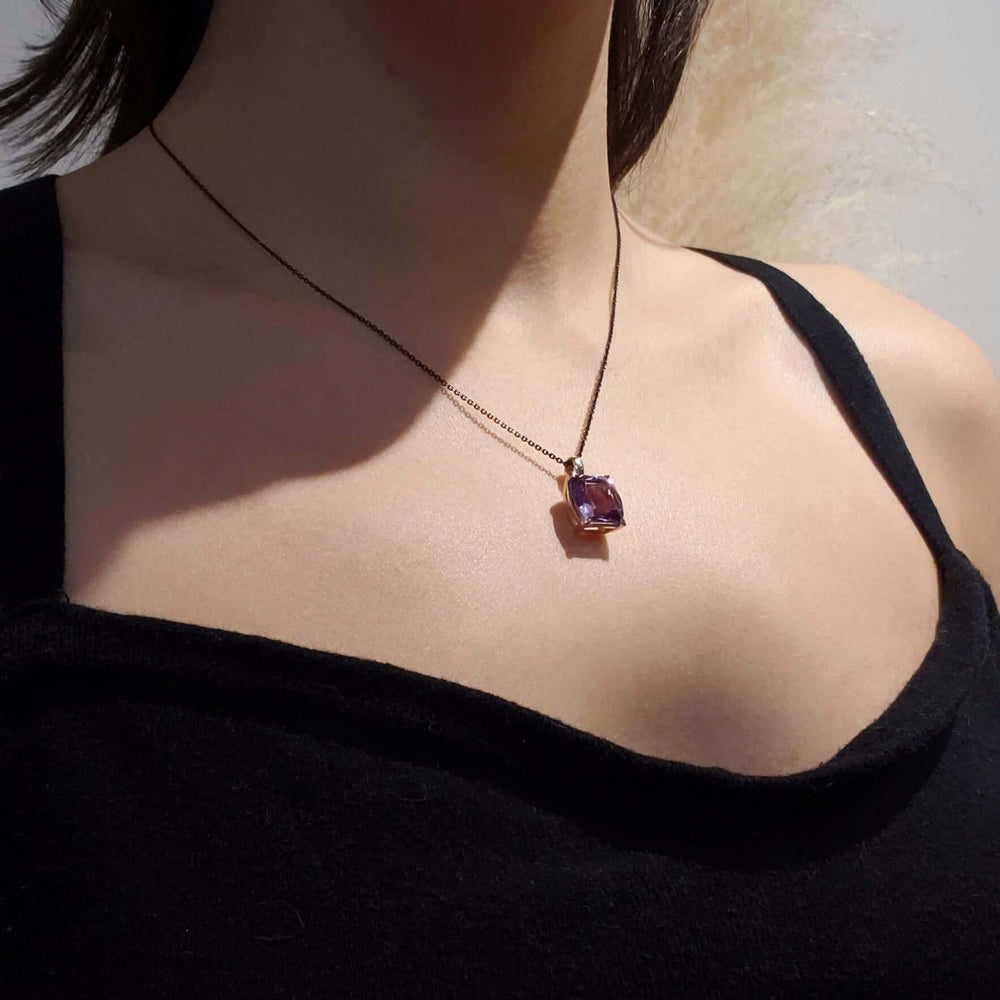 Barrel-cut amethyst pendant in yellow gold on black chain, worn on a woman's neck