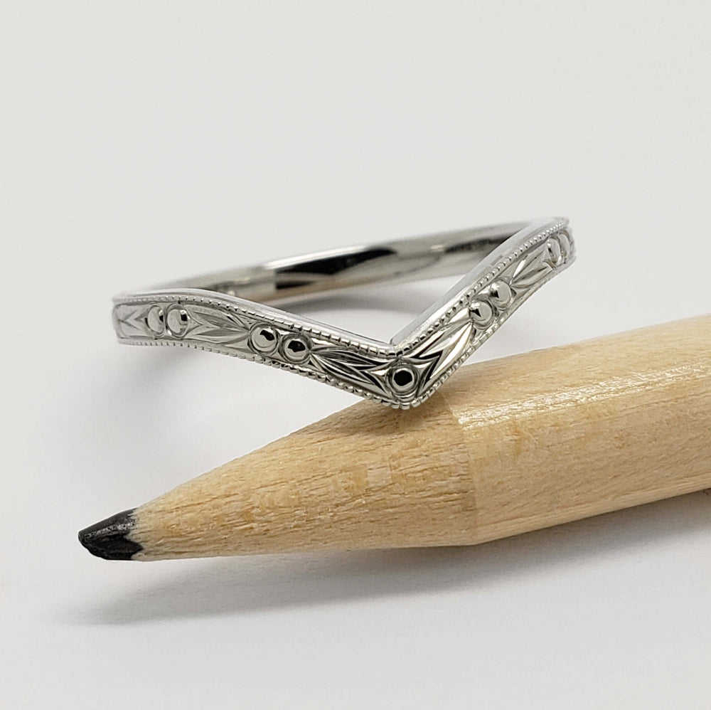 Berry Chevron II 14kt white gold wedding ring resting on a pencil, showing engraved details