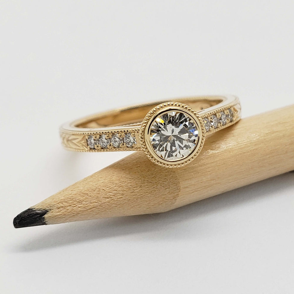 Bezel-set lab diamond engagement ring in yellow gold, displayed on a pencil