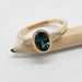 Bezel-set oval teal sapphire ring with diamond shoulders in yellow gold, displayed on pencil
