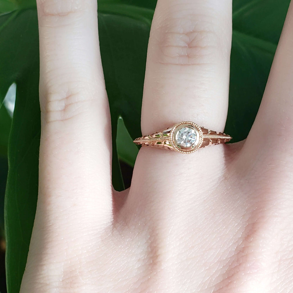 Bezel set diamond and engraved 14k rose gold ring worn on a hand