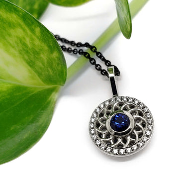 Blue sapphire and diamond halo pendant in white gold, shown with green leaf background