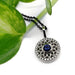 Blue sapphire and diamond halo pendant in white gold, shown with green leaf background