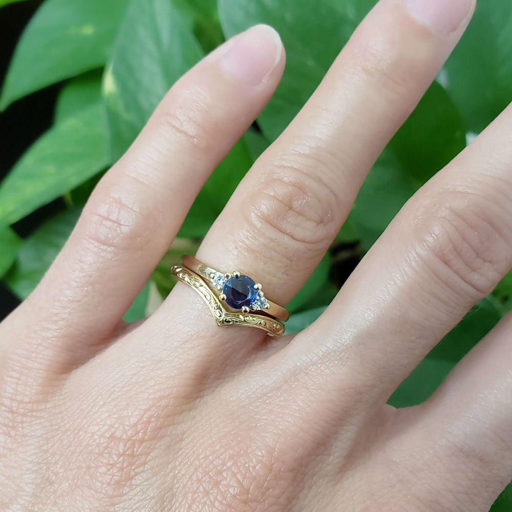 Blue sapphire and diamond engagement ring stacked with engraved yellow gold band on hand