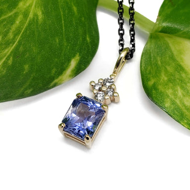 Blue sapphire and lab diamond pendant in yellow gold, displayed beside green leaf