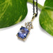 Blue sapphire and lab diamond pendant in yellow gold, displayed beside green leaf