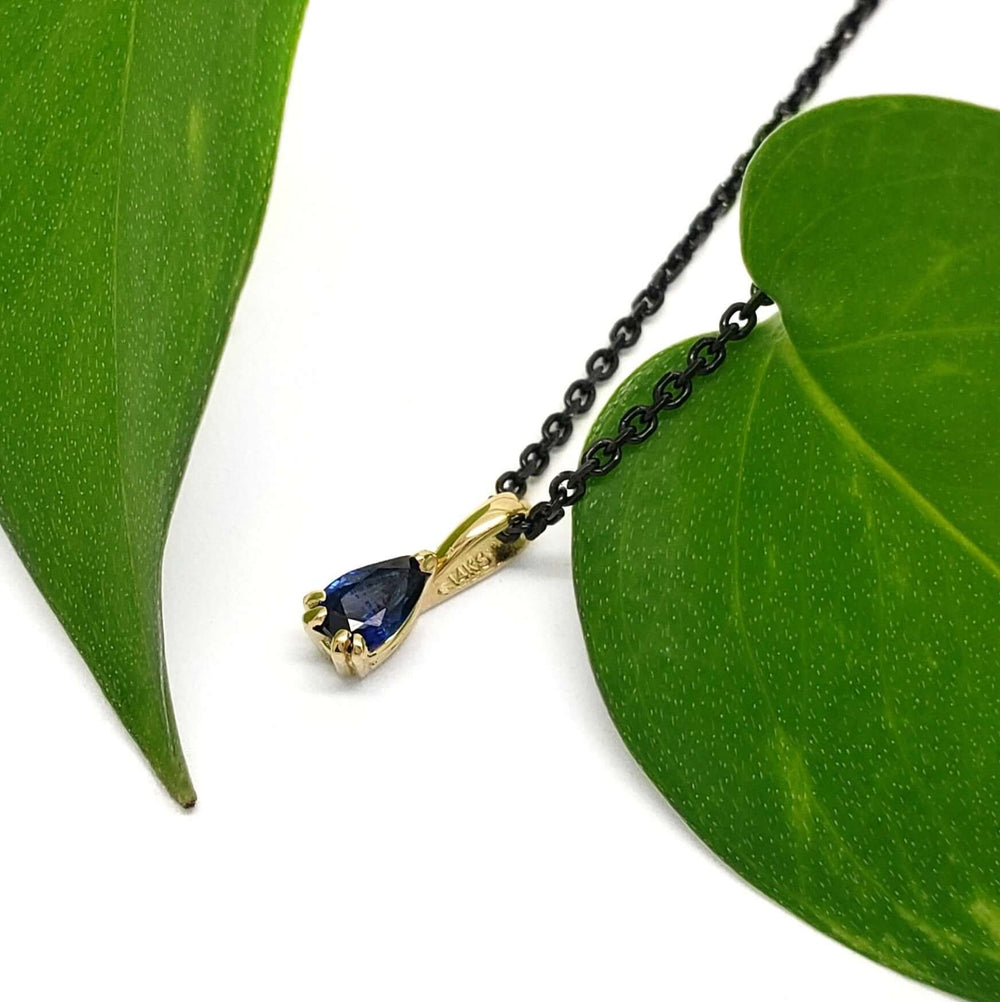 Blue sapphire and yellow gold pendant on black chain, styled with green leaves