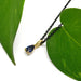 Blue sapphire and yellow gold pendant on black chain, styled with green leaves