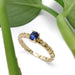 Blue sapphire engagement ring in yellow gold with wheat motif, shown with green leaves