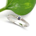 Blue sapphire stacking ring in 14k white gold with millgrain edge, shown with green leaf