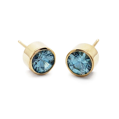 Pair of round blue zircon bezel stud earrings in 14kt yellow gold on white background