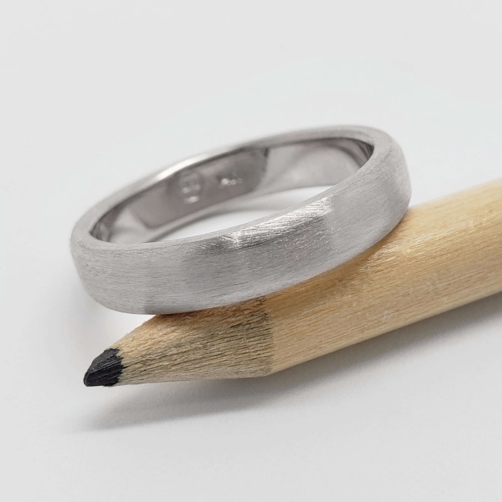 Brushed 14k white gold flat wedding ring resting on a pencil