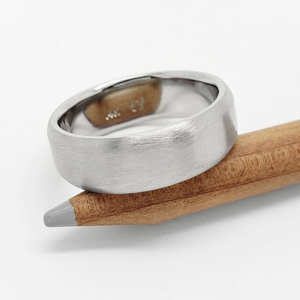 Brushed 14k white gold flat wedding ring resting on a pencil
