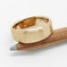 Brushed 14k yellow gold flat wedding ring resting on a wooden pencil