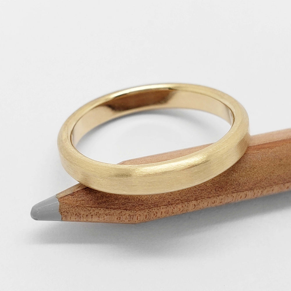 Brushed 14k yellow gold wedding band displayed on a wooden pencil