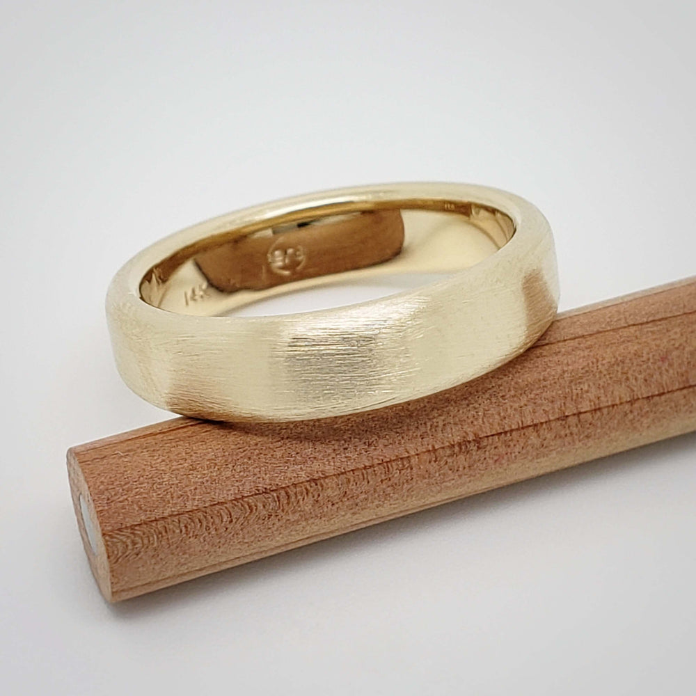 Brushed 14k yellow gold wedding band resting on a wooden stick