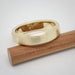 Brushed 14k yellow gold wedding band resting on a wooden stick