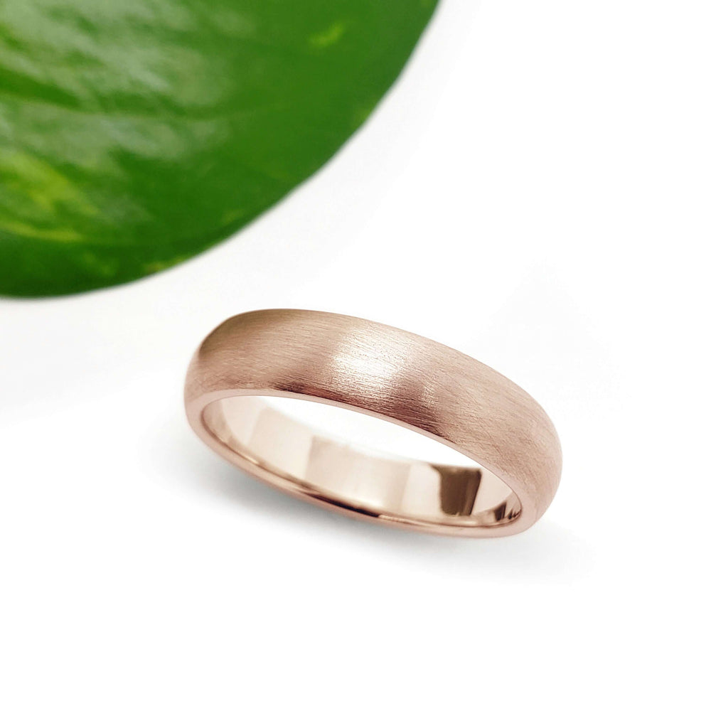 Brushed 14kt rose gold wedding band on white background with green leaf