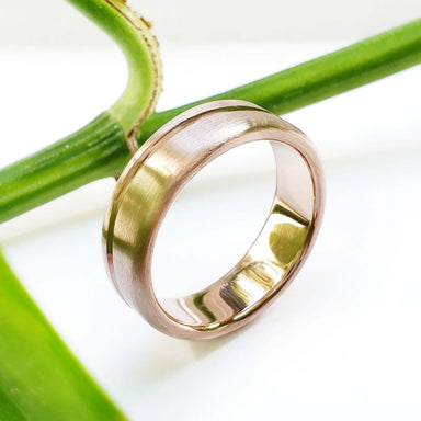Brushed 14kt rose gold wedding band with carved wave detail, shown on a plant stem