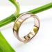 Brushed 14kt rose gold wedding band with carved wave detail, shown on a plant stem