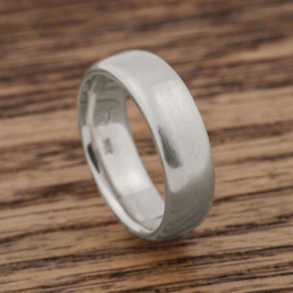 Brushed 14kt white gold flat wedding band on wood surface