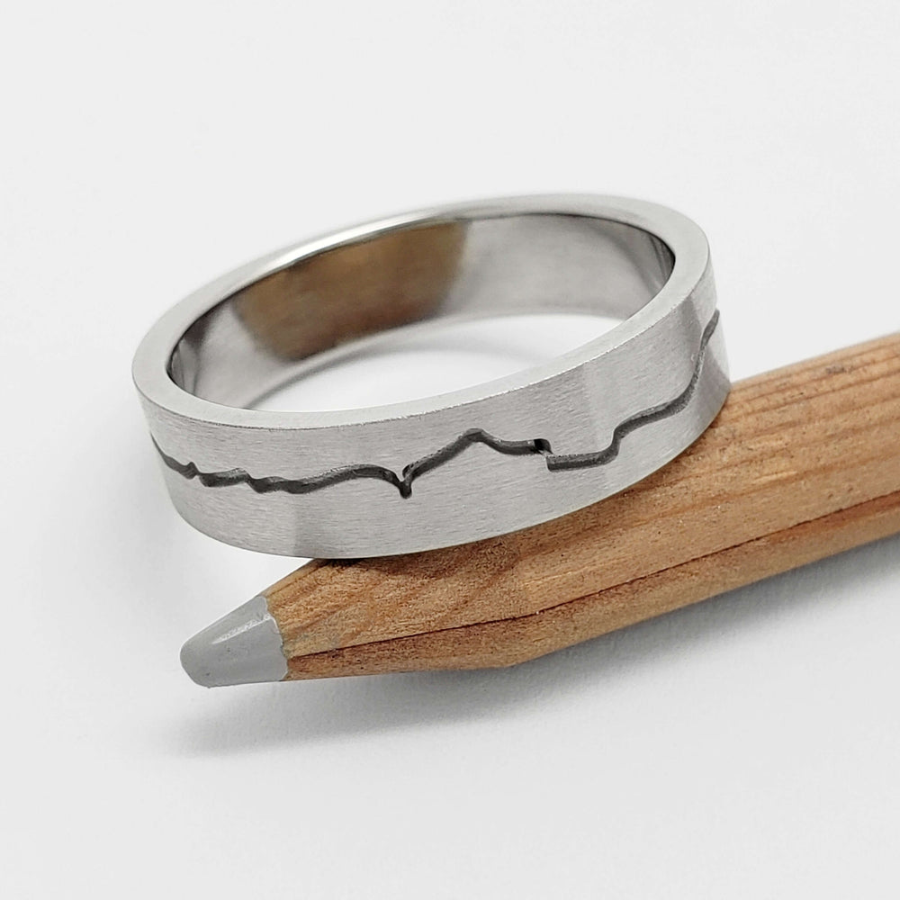 Brushed 14kt white gold mountain range wedding band resting on a wooden pencil