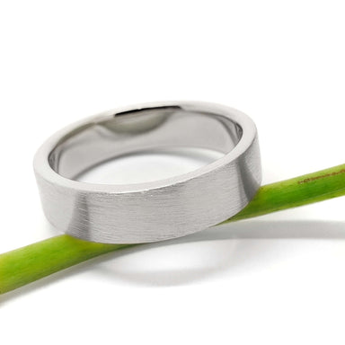 Brushed 14kt white gold wedding band with flat profile resting on a green stem