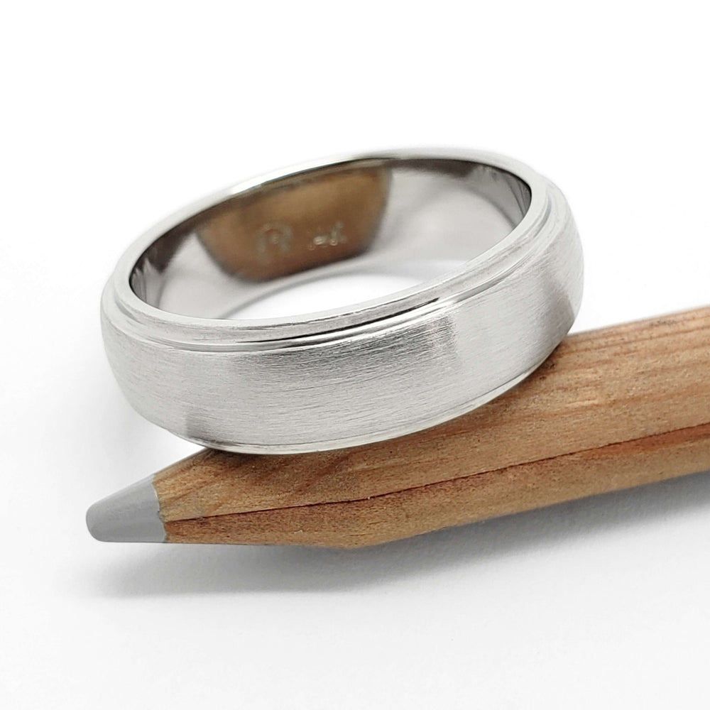 Brushed 14kt white gold wedding ring with domed step profile resting on a pencil
