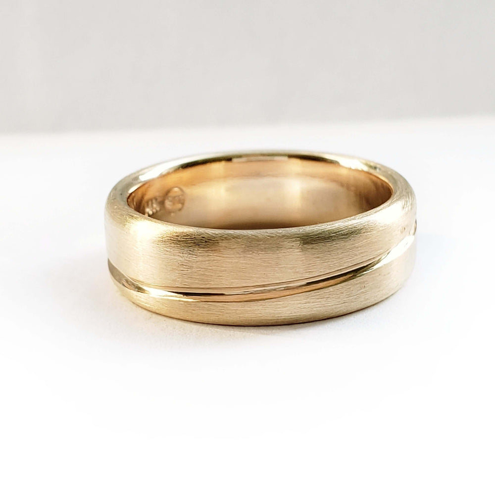 Brushed 14kt yellow gold ring with asymmetrical carved line on white background