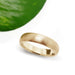 Brushed 14kt yellow gold wedding ring displayed beside a green leaf