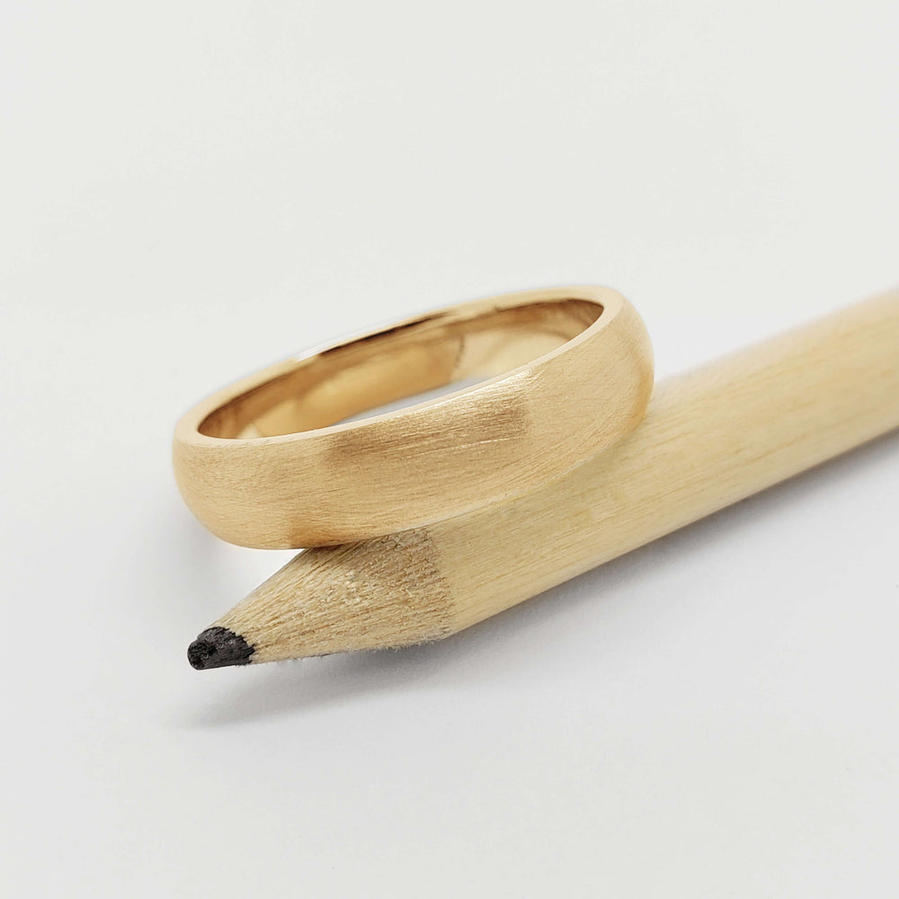 Brushed 14kt yellow gold wedding ring resting on a natural wood pencil