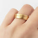 Brushed yellow gold wedding ring with carved wave detail shown on hand