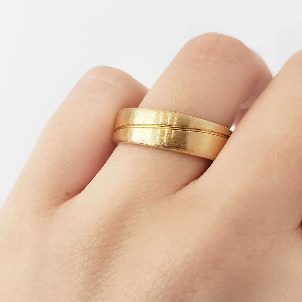 Brushed yellow gold wedding ring with carved wave detail shown on hand