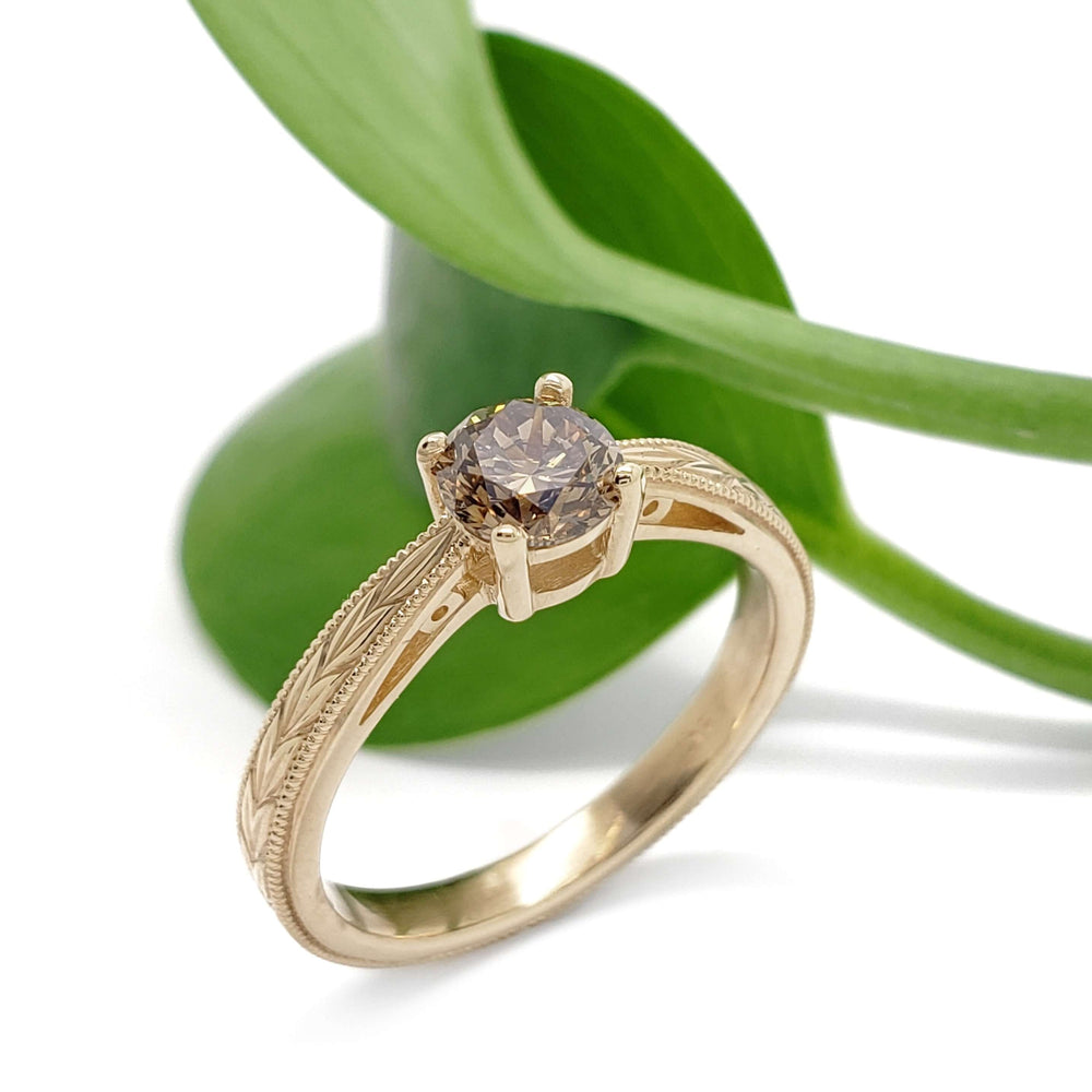 14kt yellow gold engagement ring with champagne diamond, engraved and millgrain details, beside green leaf