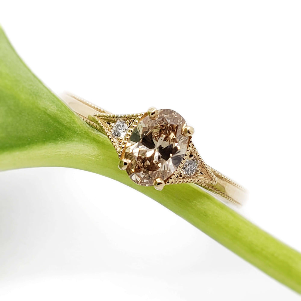 Champagne oval diamond engagement ring in yellow gold with millgrain, shown on a green stem