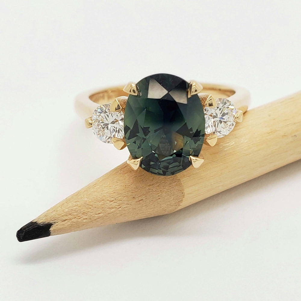 Charlotte ring with oval Australian sapphire and lab diamonds on a pencil for scale