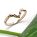 Chevron-shaped 14kt rose gold wedding ring with diamonds beside a green leaf