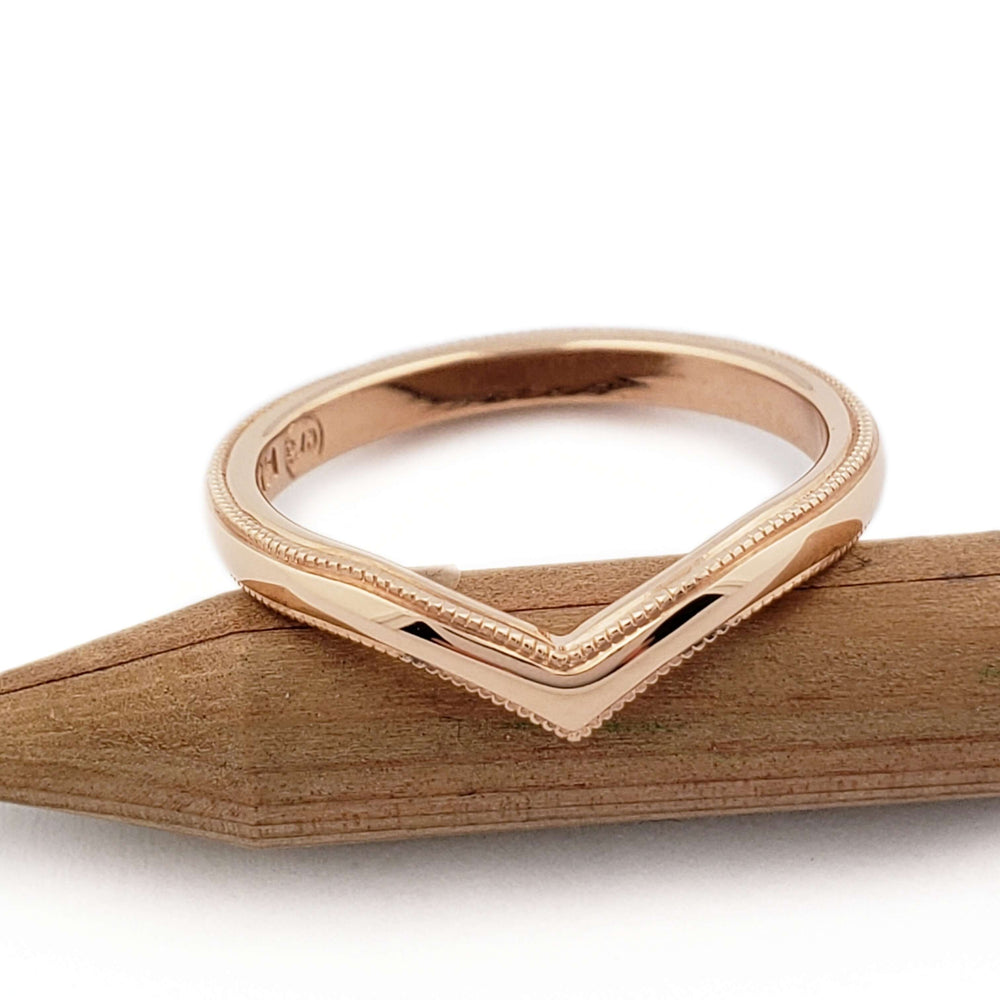 Chevron-shaped 14kt rose gold wedding ring with millgrain edge on wood