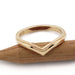 Chevron-shaped 14kt yellow gold wedding ring with millgrain, resting on wood