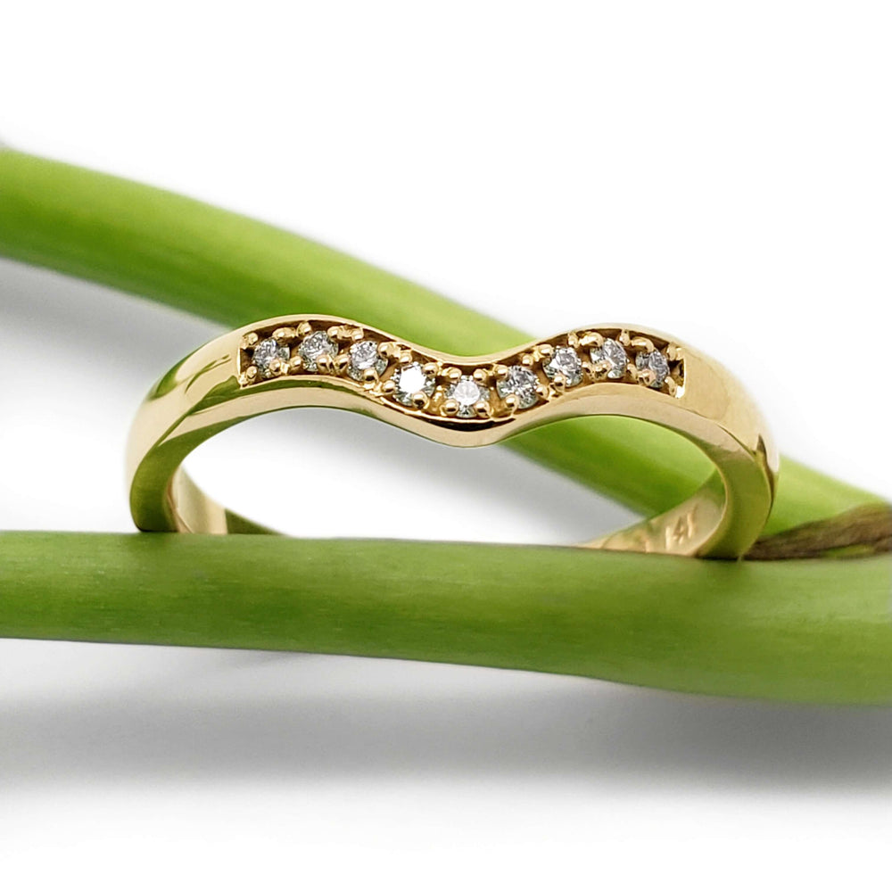 Chevron diamond wedding band in 14k yellow gold resting on green stems