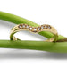 Chevron diamond wedding band in 14k yellow gold resting on green stems