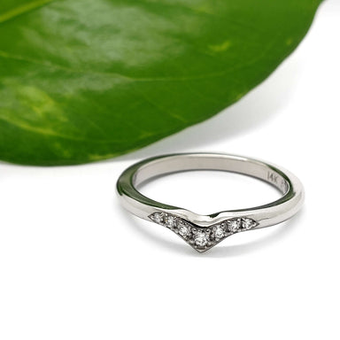 Chevron diamond wedding band in 14kt white gold beside a green leaf