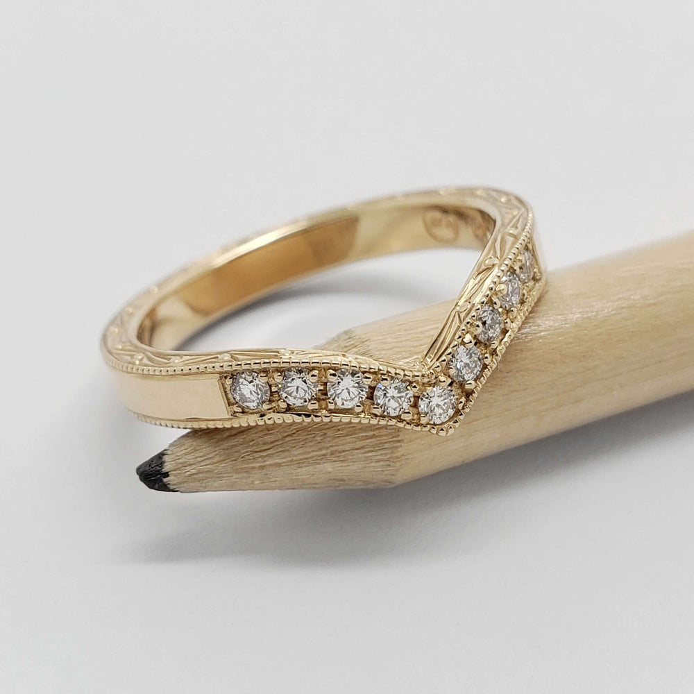 Chevron diamond wedding band in 14kt yellow gold with millgrain and engraving, shown on pencil