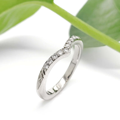 Chevron diamond wedding ring in 14kt white gold with engraved details, shown with green leaves