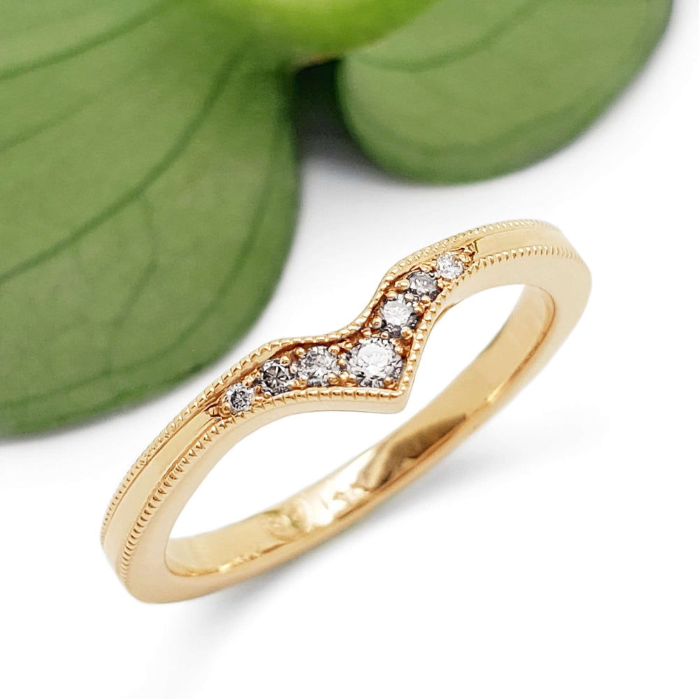 Chevron diamond wedding ring in 14k yellow gold with millgrain, shown near a green leaf