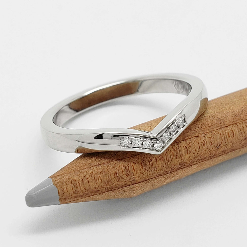 Chevron pavé diamond wedding ring in white gold resting on a wooden pencil
