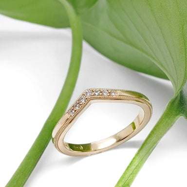 14kt yellow gold chevron wedding band with lab diamonds, shown with green leaves