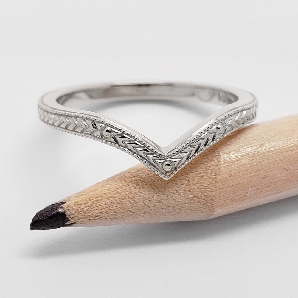 Chevron wedding ring in 14kt white gold with engraved detail, shown on a pencil
