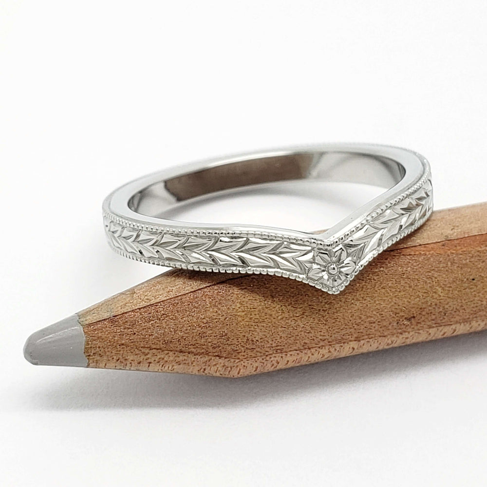 Chevron wedding ring in 14kt white gold with engraved floral and wheat pattern, shown on pencil