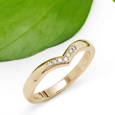 Chevron wedding ring in yellow gold with pavé diamonds beside a green leaf